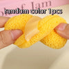 A hand holds a yellow exfoliating cleansing sponge with a light beige ribbon, showing its texture and size.