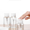 Three clear glass refillable pump dispenser bottles of liquid sitting on a wooden surface.