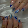 Nahaufnahme langer Acryl-Nägel mit blau-weizem Blumenmuster und goldenen Akzenten.