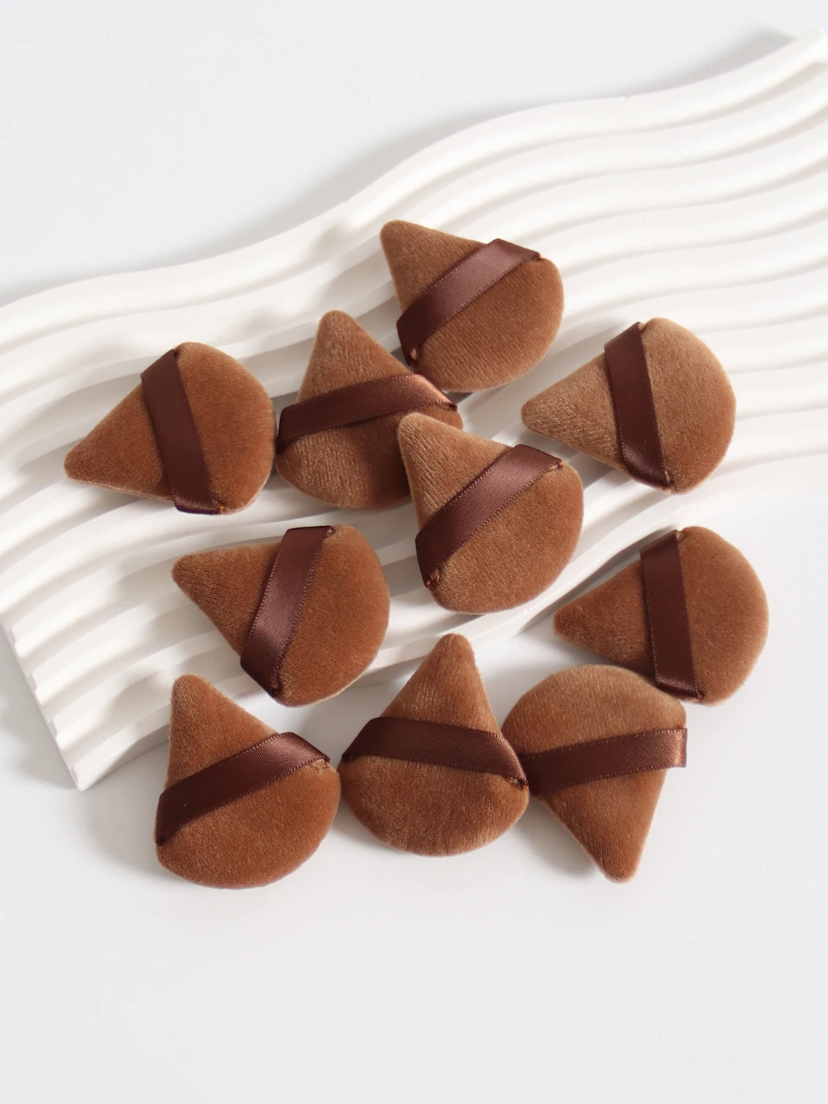 Un ensemble de touffes de poudre brunes triangulaires avec des accents de ruban brun foncé, arrangées sur une surface blanche