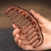 A hand holds a natural golden sandalwood wide-tooth detangling comb with curved teeth.