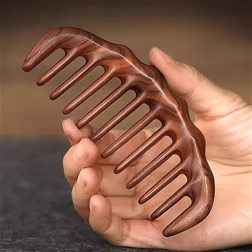 A hand holds a natural golden sandalwood wide-tooth detangling comb with curved teeth.
