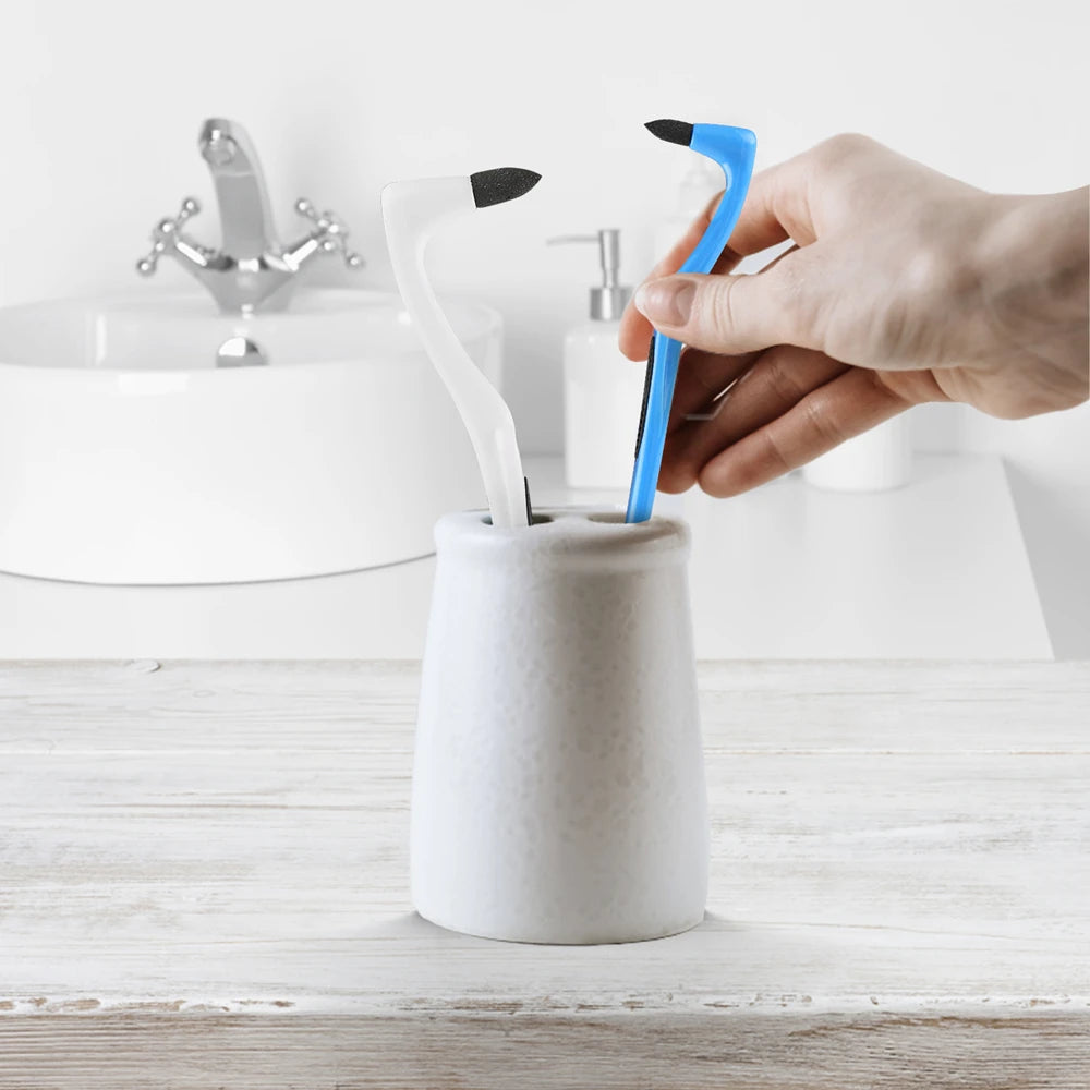 A hand holds a white ceramic tube containing a manual tooth stain remover with an interdental brush.