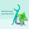 A teal dental floss pick with a curved handle is shown next to a piece of mint leaves.