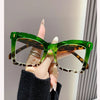 A hand holds a pair of green-framed reading glasses with tortoiseshell lenses against a light background.