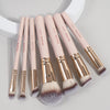 A set of seven pink makeup brushes with gold ferrules and fluffy synthetic bristles arranged diagonally on a light gray surfa