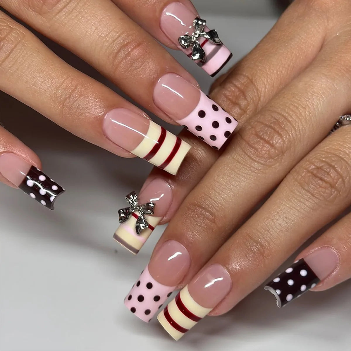 A close-up of hands displaying gothic Y2K press-on nails featuring cross and bow designs in pink, white, and black polka dots