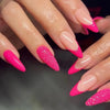 Close-up of hands displaying vibrant pink and glitter press-on false nails with a French wavy design.