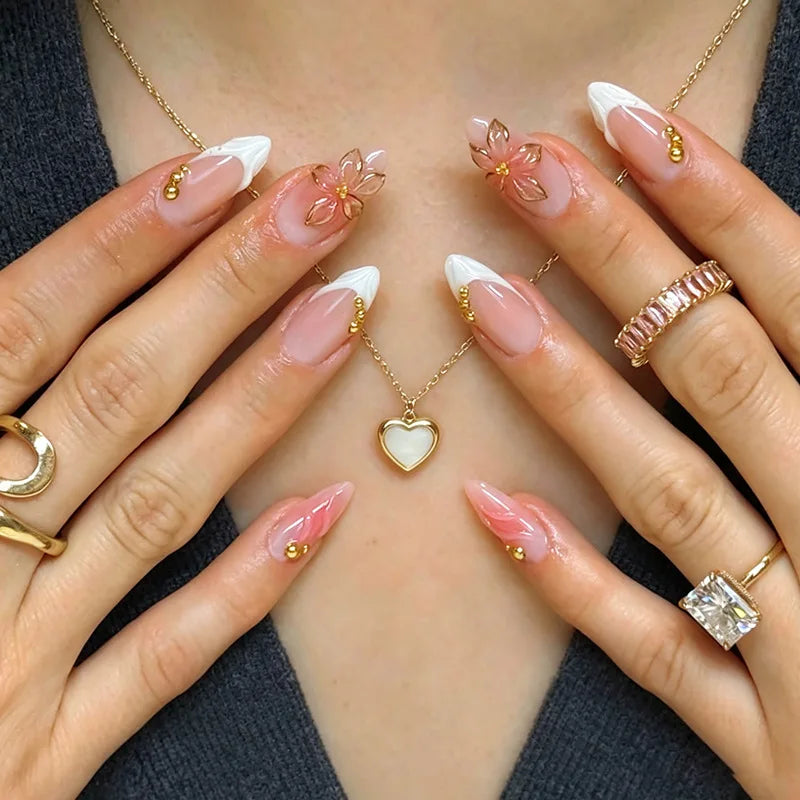 A close-up of hands displaying 24-piece almond press-on nails with floral and butterfly designs and gold jewelry.