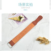 A brown leather sharpening strop is shown lying on a white marble surface next to some dried plant material.