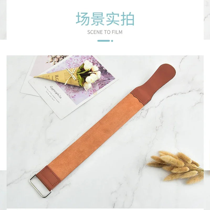 A brown leather sharpening strop is shown lying on a white marble surface next to some dried plant material.