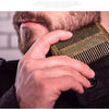 A hand is using a gold boar bristle beard and mustache comb on a man's face.