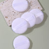 Un set de cinco esponjas de maquillaje blancas sobre una losa de mármol beige claro.