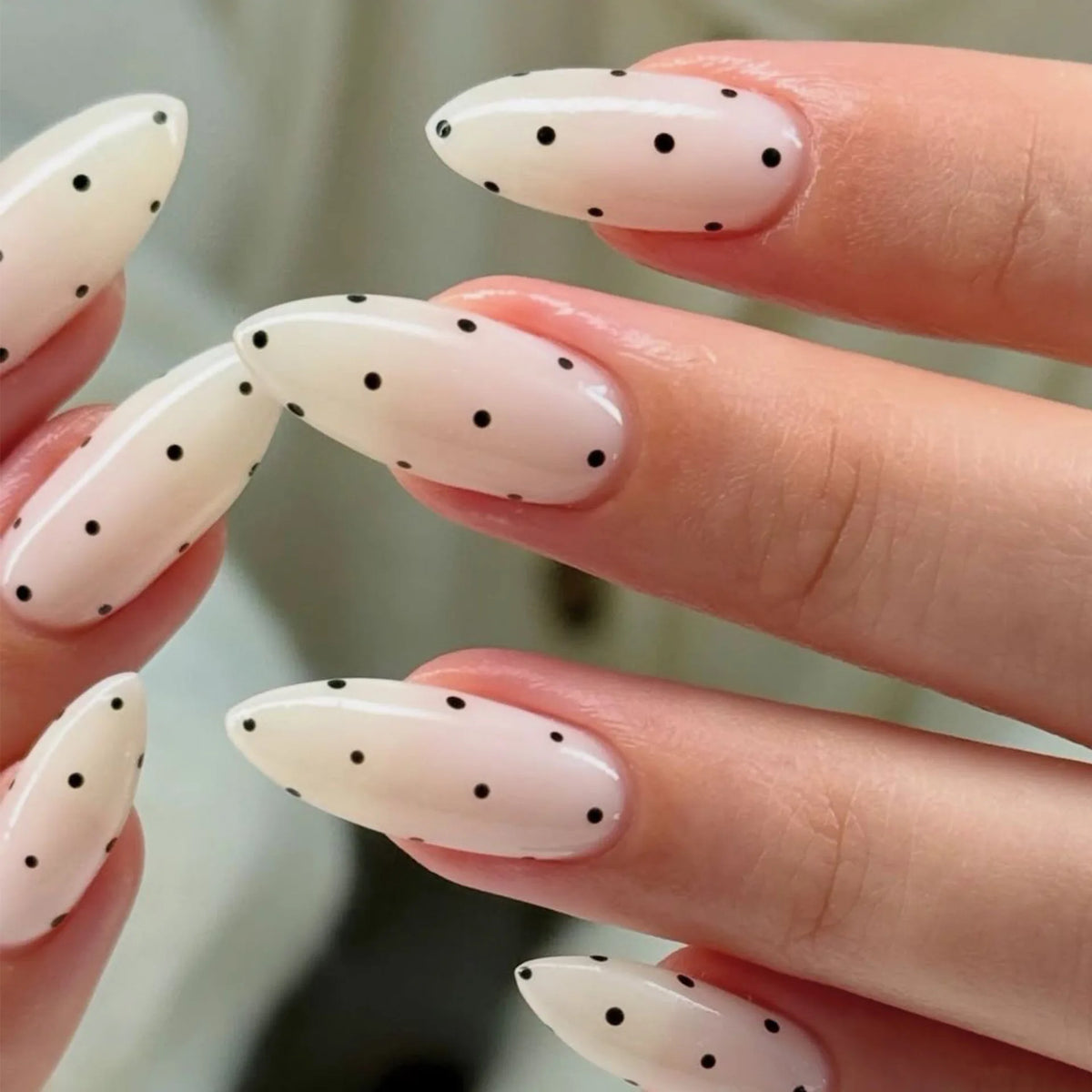 Close-up of fingers displaying reusable press-on nails with an almond shape and white base decorated with small black polka d