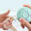 A hand is holding a light green electric baby nail trimmer with a white nozzle, demonstrating its use.