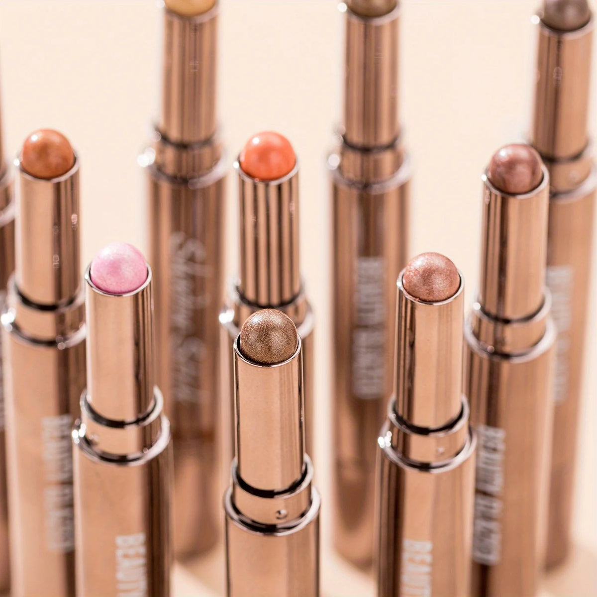 A row of metallic bronze eyeshadow sticks with double brushes displayed vertically.