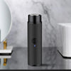 A black portable electric shaver with a textured body and a blue light indicator is shown on a marble surface.