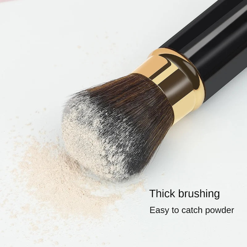 Un pinceau de maquillage rétractable noir et or avec des poils épais à côté de poudre libre.