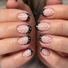 Close-up of a hand displaying reusable press-on nails with an almond shape featuring white polka dots on a black background.