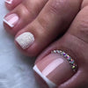 A close-up of a hand displaying press-on fake nails with short square French tips and glitter accents on the nails.