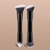 A set of two black makeup brushes with silver bristles displayed against a beige background.