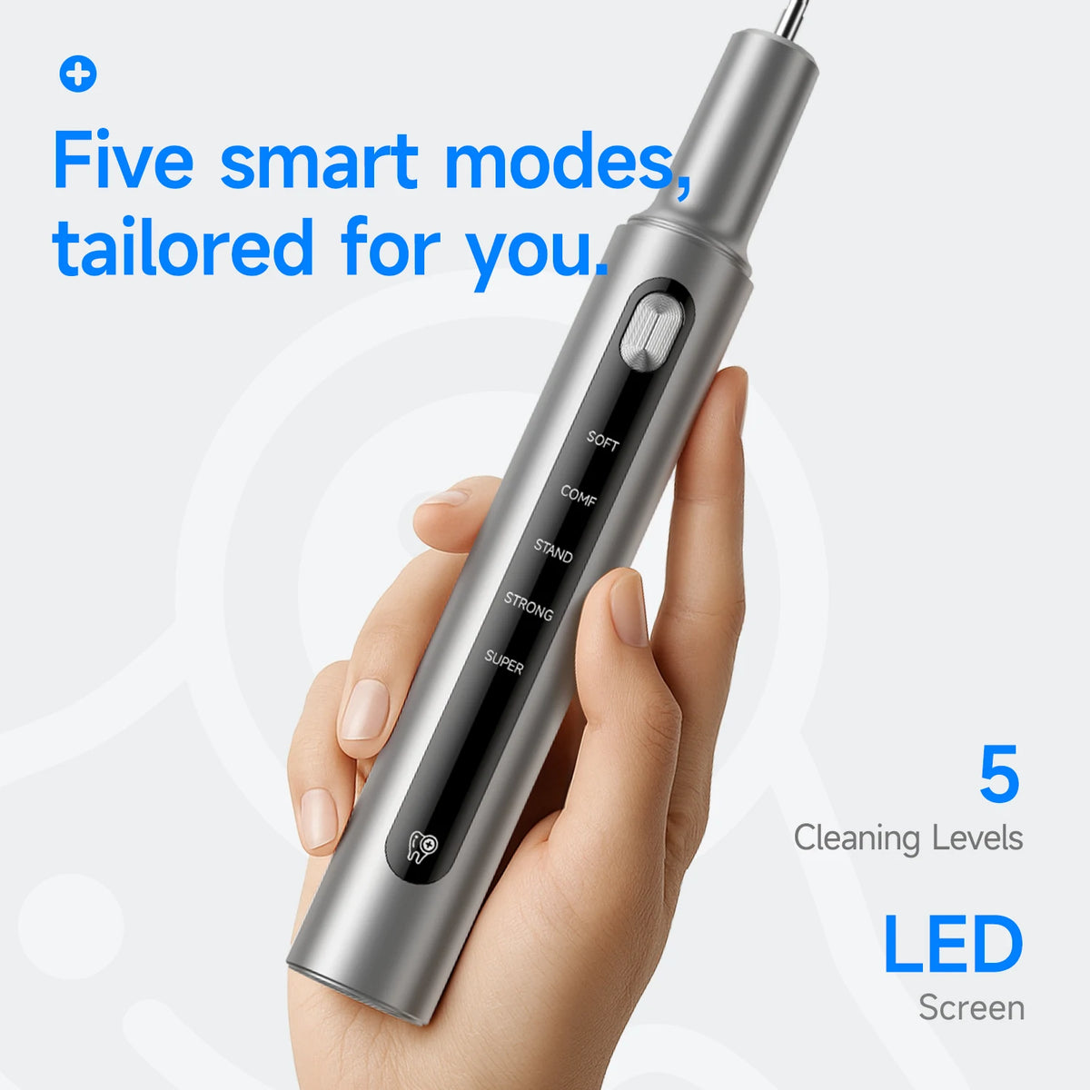 A hand holds a silver ultrasonic electric dental cleaner device with various mode settings visible on the body.