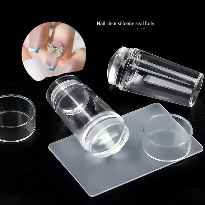 A clear silicone nail art stamper and scraper set shown on a white tray with a fingernail for scale.
