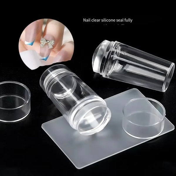 A clear silicone nail art stamper and scraper set shown on a white tray with a fingernail for scale.