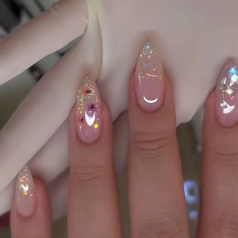 Gros plan d'une main montrant deux ongles press-on à noisette française roses avec accents scintillants.