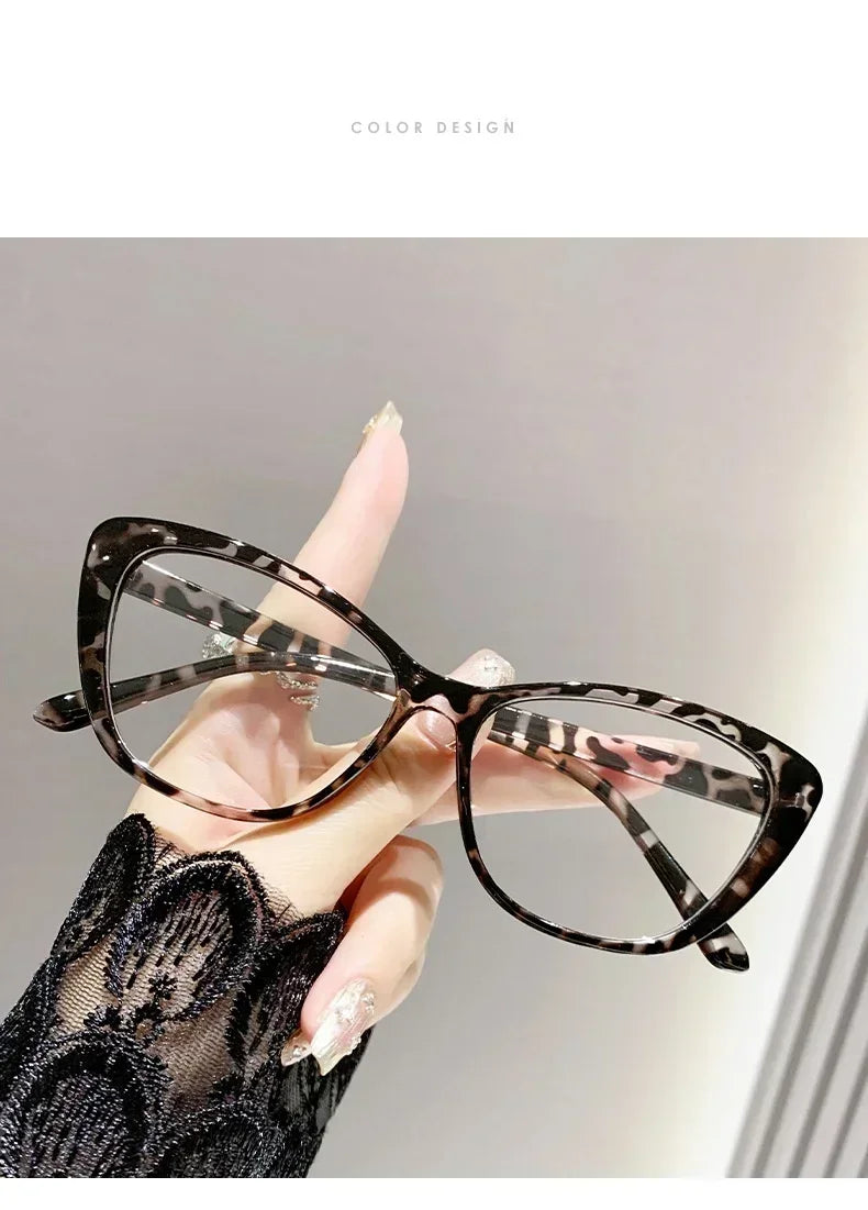 A hand is holding a pair of black and white patterned cat eye reading glasses against a light gray background.