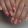 A close-up of a hand displaying press-on acrylic nails decorated with pink and yellow floral designs.