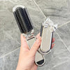 A hand holds a silver folding mini hair comb with a mirror for styling