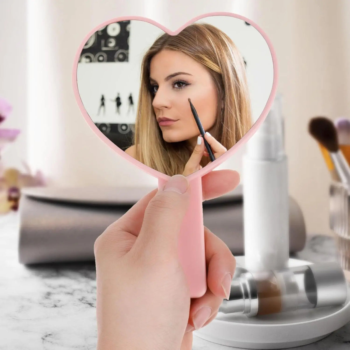 Une main tient un miroir en forme de cœur rose reflétant le visage et les cils d'une femme.