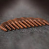 A close-up of a natural golden sandalwood wide-tooth detangling comb resting on a dark surface.