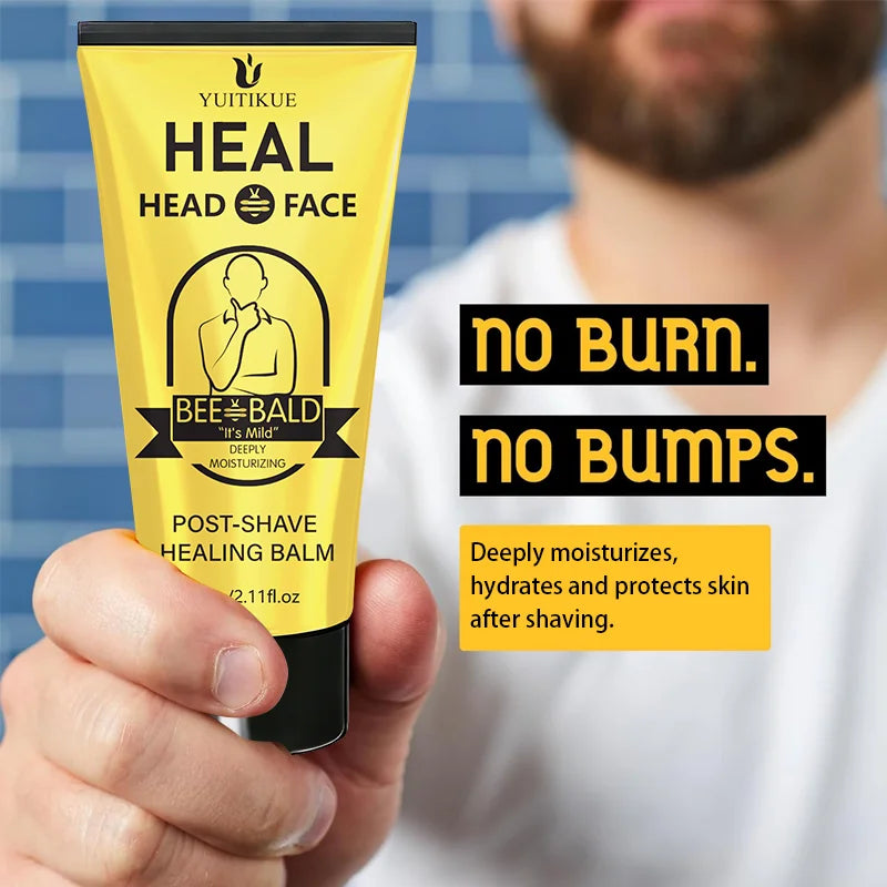 A yellow tube of Bee Bald Post-Shave Healing Balm is held by a hand against a blurred blue background.