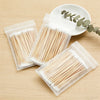 A collection of precision wooden cotton swabs in clear plastic packaging are displayed on a light wooden surface.
