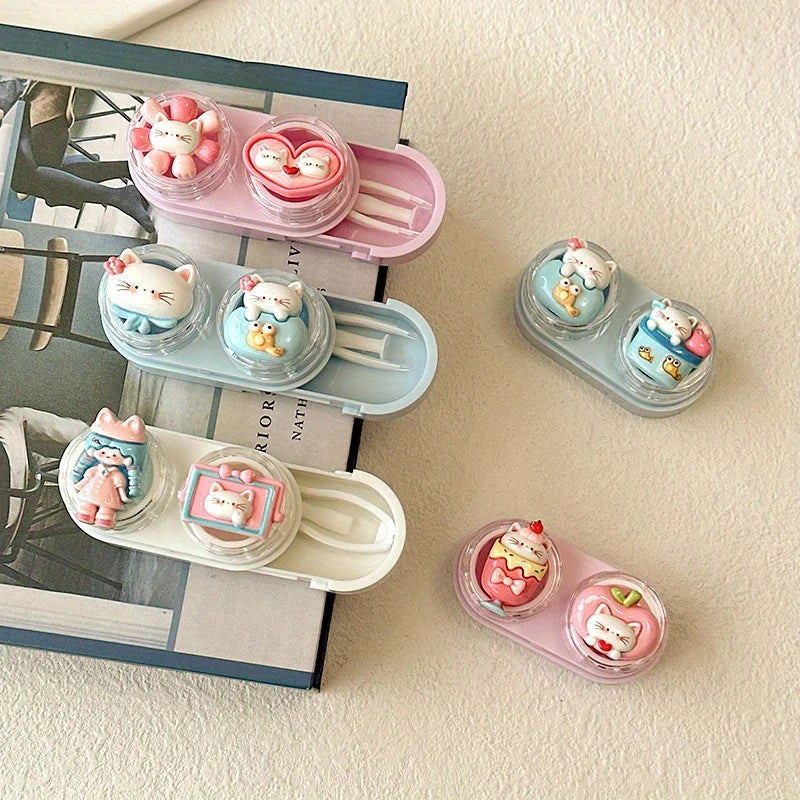 Eine Sammlung von rosa und blauen tragbaren Cartoon-Katzen-Kontaktlinsenbehältern auf einer weißen Oberfläche.