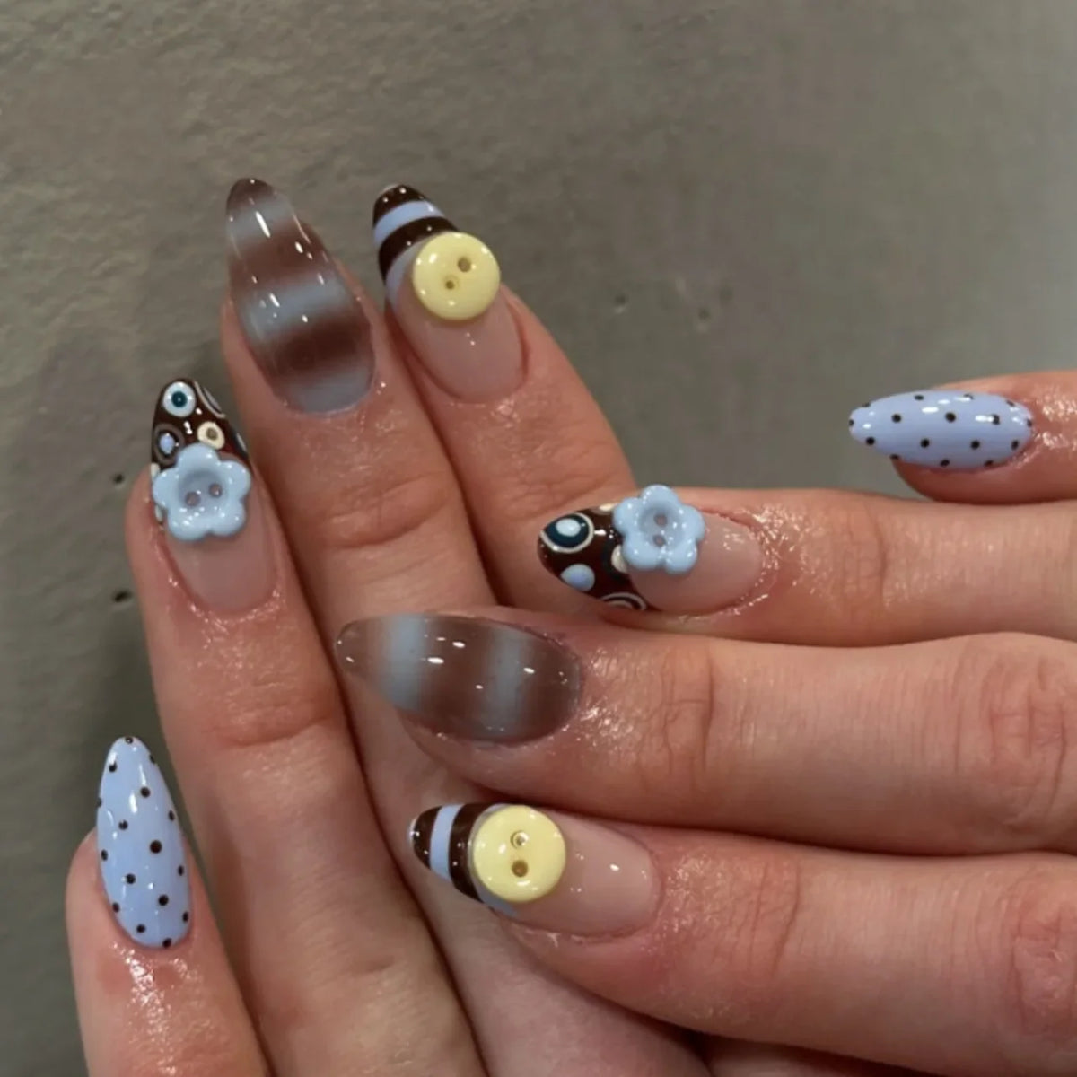 Gros plan d'une main montrant des kits de faux ongles en forme de fleur à amande avec des pois marron, blanc et bleu clair.