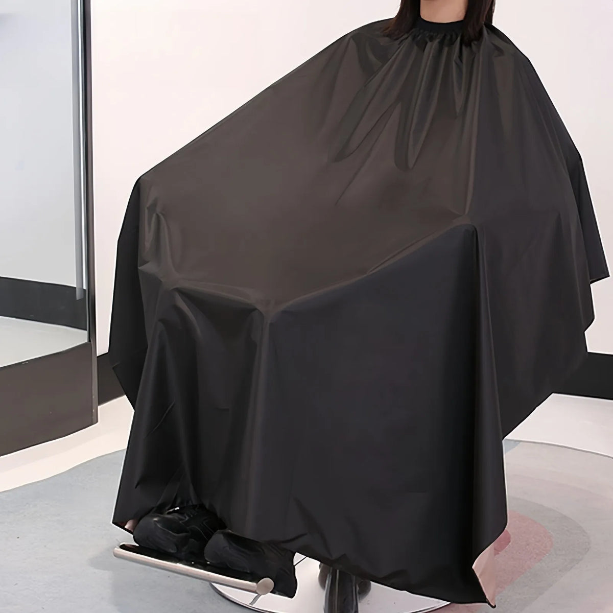 Une cape professionnelle noire pour couper les cheveux, drapée sur un mannequin.
