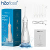 A white portable oral irrigator device is shown next to its packaging and accessories on a reflective surface.
