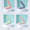 Four variations of a portable folding hairbrush in pink, blue, green, and beige colors displayed on white stands.