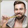 Ein Mann hält eine natürliche Holzmiswak-Zahnbürste und lächelt, mit einem Handtuch um den Hals.