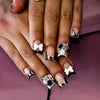 A close-up of hands displaying a set of nude pink press-on nails featuring leopard print and 3D floral charms.