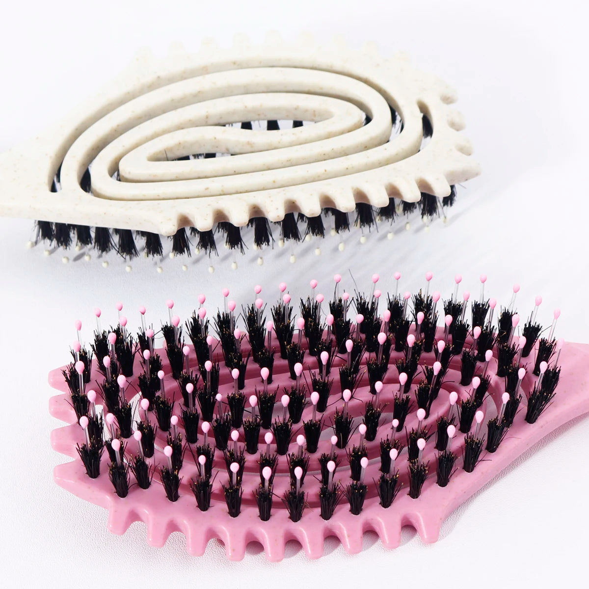 A pink silicone styling comb with black bristles is shown next to a white spiral comb.