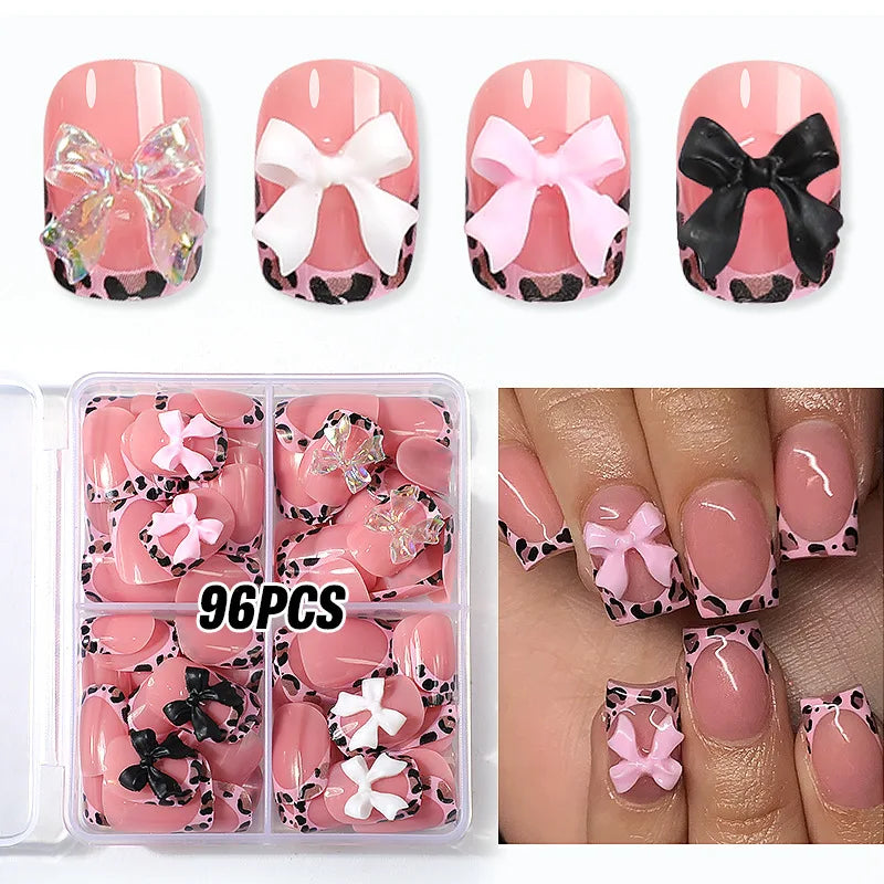 A set of 96 leopard print press-on nails in pink and black with white bow accents displayed on fingernails.