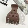 A brown root lifting hair clip with multiple prongs and holes is shown on a white surface.