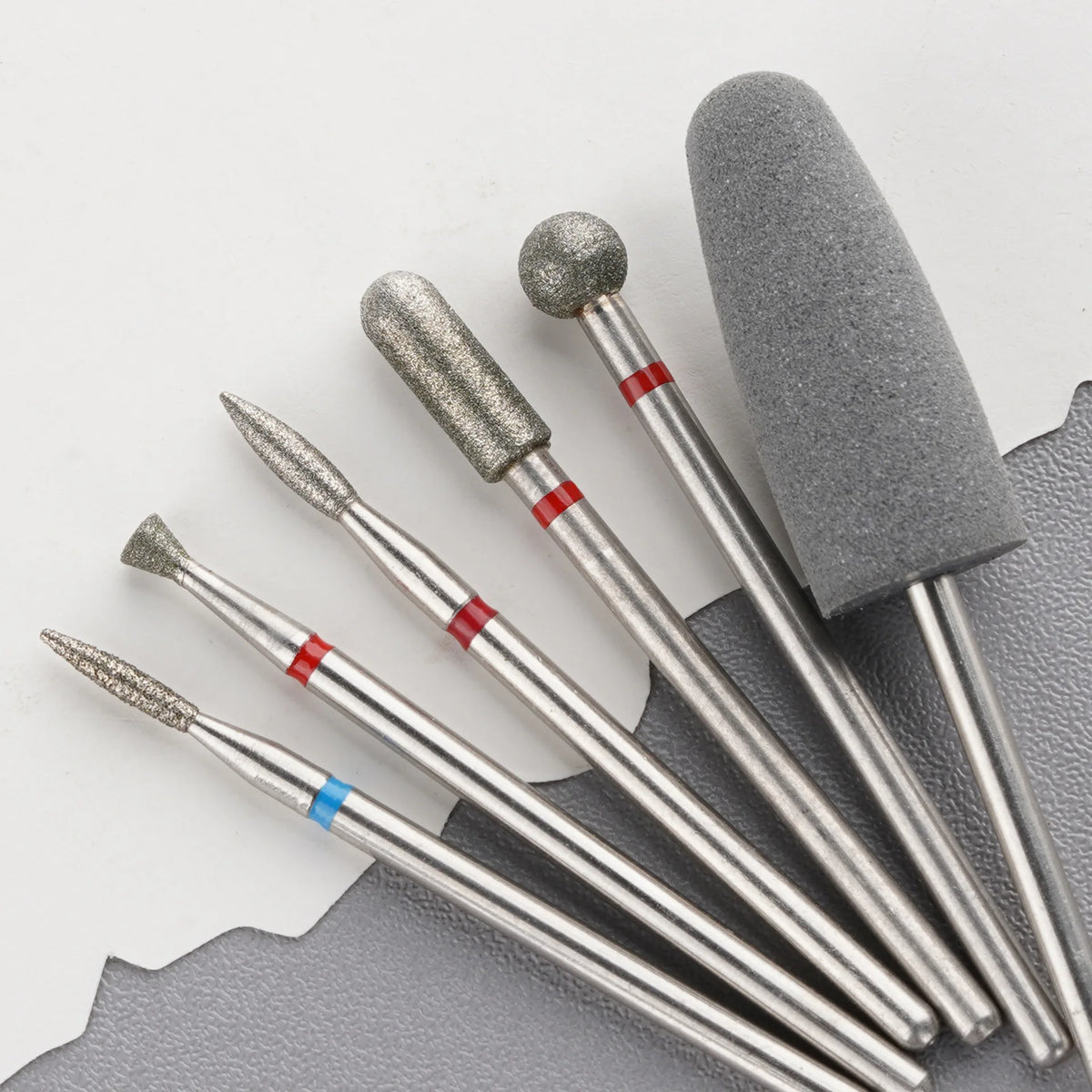 Set professioneller Diamant-Sand-Nagelfeilen mit silbernen und grauen Griffen auf dunkler Oberfläche.