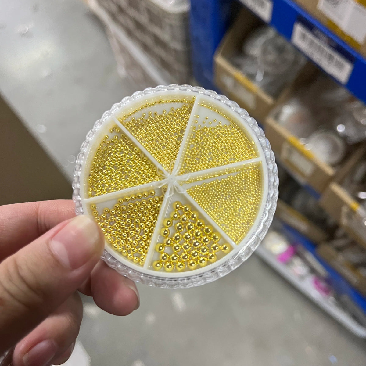 A hand holds a circular clear plastic decoration with various gold-colored stainless steel beads for nail art.