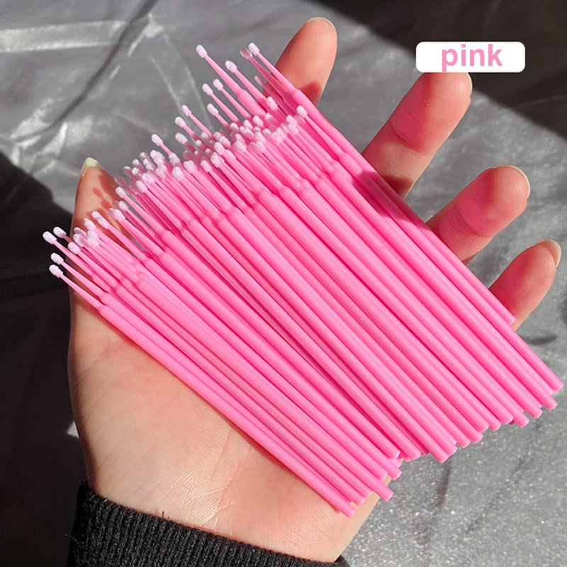Une main tient un paquet de pinceaux de nettoyage et d'extension pour cils roses.