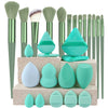A complete makeup brush set featuring various sizes of green and teal synthetic brushes and sponges.